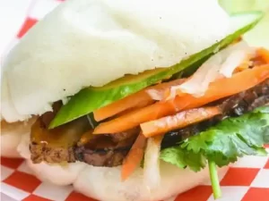 A bun with meat, sliced carrots, and lettuce