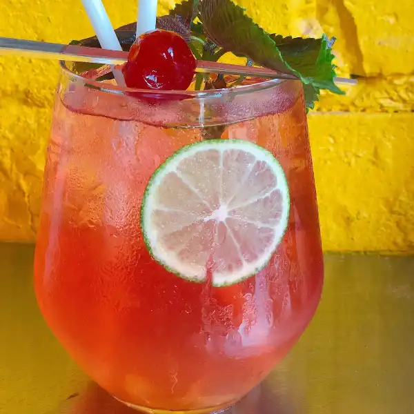 Cocktail glass with red liquid, cherry, ice, and lemon