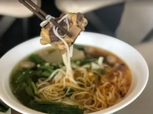 Bowl of Oxtail Pho with bone and meat held in chopsticks